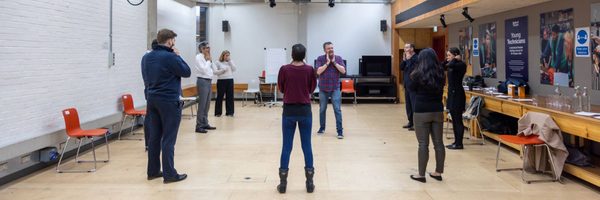 A group of people in a workshop setting, all standing and facing each other